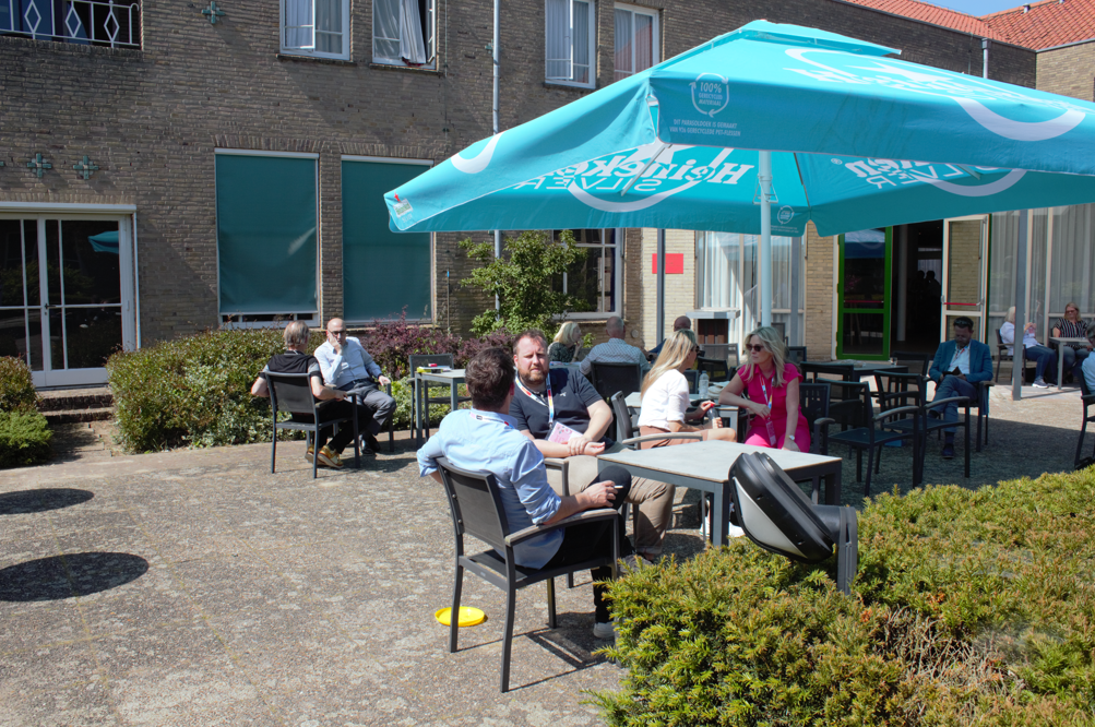 Festival guests continue conversations at courtyard tables beneath a turquoise canopy.