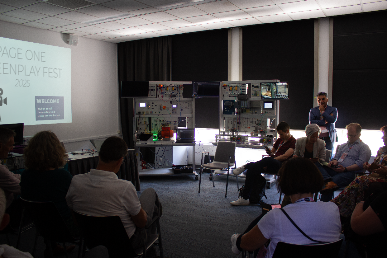 A presenter and seated participants take part in a screenplay workshop beside a technical media installation.
